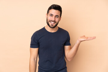 Caucasian handsome man isolated on beige background holding copyspace imaginary on the palm to...