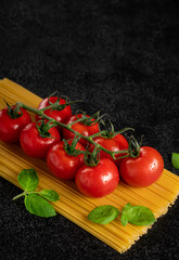 pasta spaghetti and tomatoes on a branch on a dark background top view. Vertical orientation, copy space