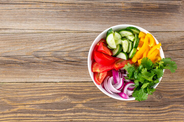 Plate of rainbow salad with different vegetables and herbs in white bowl on wooden background