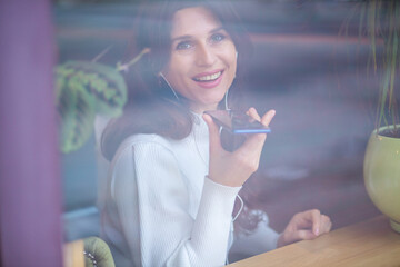 Shot through glass, a beautiful young European woman with headphones and a phone in her hands...