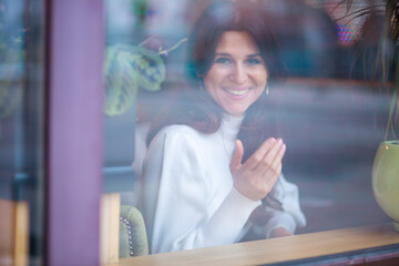 Shot through glass, a beautiful young European woman with headphones and a phone in her hands...
