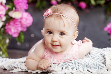 Portrait of a beautiful little baby girl with pink flowers. Sweet smiling girl lying on her stomach