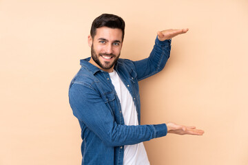 Caucasian handsome man isolated on beige background holding copyspace to insert an ad
