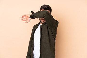 Caucasian handsome man isolated on beige background covering eyes by hands