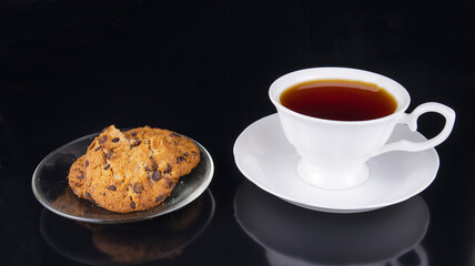 white cup of tea with oatmeal cookies on black background