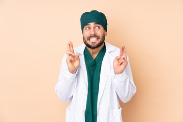 Surgeon man isolated on beige background with fingers crossing