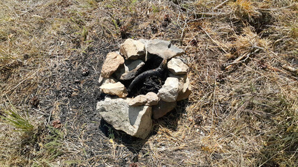 An extinct bonfire surrounded by rocks on the ground under the open sky in nature. Camping trips and picnics. Tourist holidays. The concept of a forest fire.