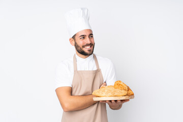 Male baker holding a table with several breads isolated on white background laughing