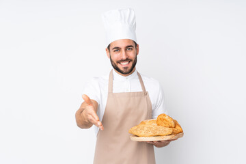 Male baker holding a table with several breads isolated on white background handshaking after good deal