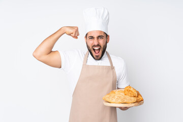 Male baker holding a table with several breads isolated on white background celebrating a victory
