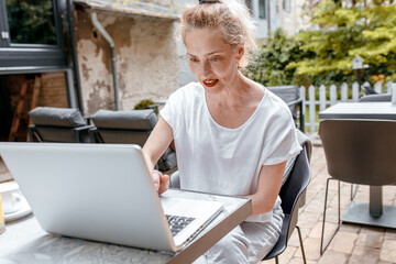 Senior female blogger in casual wear sitting in coffee shop using laptop.