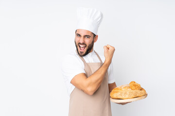 Male baker holding a table with several breads isolated on white background making strong gesture