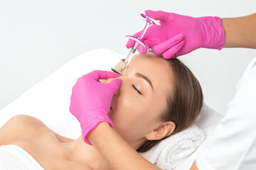 Obraz na płótnie Canvas The doctor does injections to correct the hump on the nose with the beauty of the blonde. The beautician doees injections against wrinkles on the face. Women's cosmetology in a beauty salon.