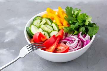 Plate of rainbow salad with different vegetables and herbs in white bowl on grey stone background