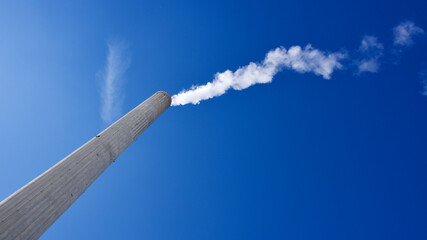 High smoke chimney in front of the blue sky. Central heating chimney. White smoke coming out of the...