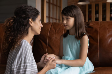 Loving young Latino mother talk speak with little 8s daughter, help with school problems. Caring...
