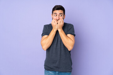 Caucasian handsome man nervous and scared putting hands to mouth over isolated purple background