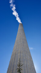 Obraz premium High smoke chimney in front of the blue sky. Central heating chimney. White smoke coming out of the chimney.