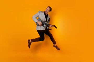 Fototapeta na wymiar Stylish and cool guy in a suit and with a game guitar on a yellow background, playing and dancing, jump shot in motion. have fun and have a good time