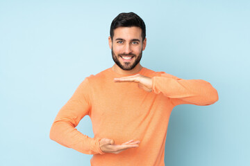 Caucasian handsome man holding copyspace imaginary on the palm to insert an ad over isolated blue...