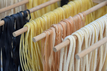 selbstgemachte frische Pasta in verschiedenen Farben hängen zum Trocknen auf einer Holzstange