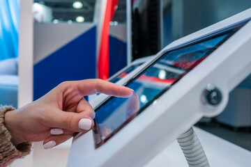 Woman hand using touchscreen display of interactive floor standing white tablet kiosk at exhibition...