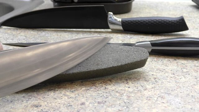 Sharpening a knife on a whetstone by hand. A man's hand drives a knife over a whetstone.
