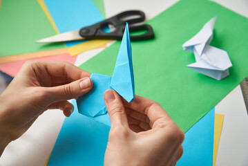 DIY concept. Woman make origami easter rabbit from color paper. Origami lessons