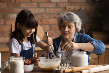 Caring senior Hispanic grandmother and little 8d granddaughter have fun baking cookies at home...