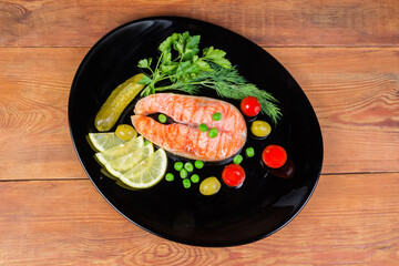 Fototapeta na wymiar Grilled salmon steak with vegetables and greens on black dish