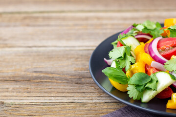 Plate of rainbow salad with different vegetables and herbs on black plate on wooden background