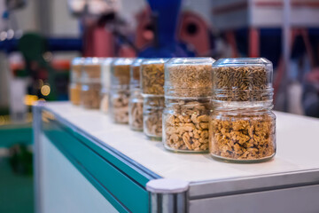 Different kinds of pelleted compound feed, fodder in glass jars: before and after extrusion - food for domestic animals at agricultural exhibition, trade show: close up. Agriculture, husbandry concept