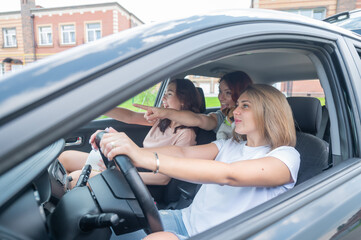 Three friends go on a trip. Caucasian women drive in a car and point fingers in surprise.