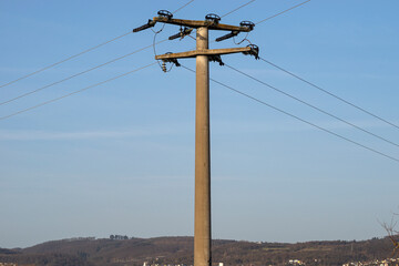 Concrete electric pole with ceramic insulators and voltage lines, in background blue sky with blue...