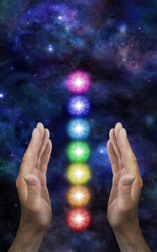 Sending Distant Healing to the Seven Chakras - male parallel hands with a neat stack of seven rainbow coloured chakra vortexes between against a dark deep space background with copy space
