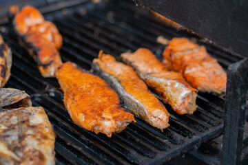 Process of cooking salmon steaks and mackerel fish on grill at summer local food market - close up. Outdoor cooking, barbecue, gastronomy, seafood, cookery, street food concept