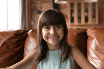 Close up headshot portrait of happy small 8s Latino girl child have webcam online talk on gadget at...