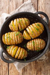 hasselback potatoes are thinly sliced potatoes that are baked to golden brown perfection with butter and garlic closeup in a pan on the table. Vertical top view from above