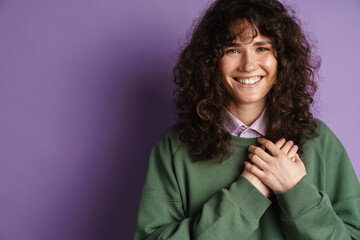 Happy brunette curly girl smiling and holding her hand at chest