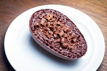 Stuffed chocolate easter egg with grated chocolate on the top on a white plate on a wood table.