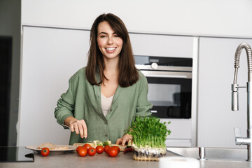 Joyful brunette woman smiling while preparing sandwich with avocado
