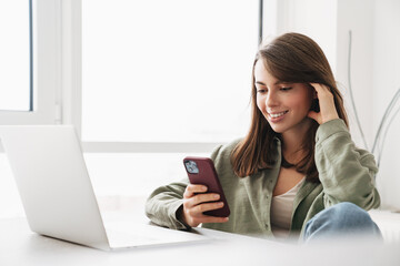 Smiling woman using cellphone while working with laptop