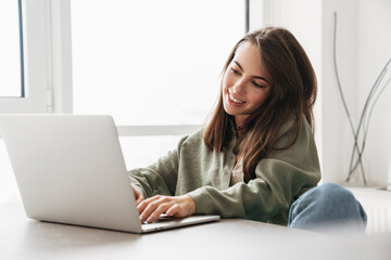 Fototapeta premium Smiling woman talking on cellphone while working with laptop