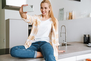 Happy blonde woman smiling while taking selfie photo on cellphone