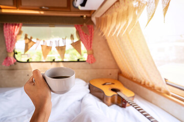 Fototapeta na wymiar Young woman traveler with cup of coffee laying in camper van and looking beautiful landscape while road trip traveling on vacation