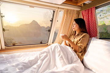 Young woman traveler with cup of coffee laying in camper van and looking beautiful landscape while...