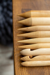 Assorted wooden knitting needles lie on a wooden table, in the background a blurred gray plaid merino wool