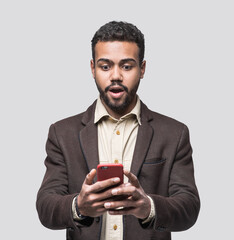 Portrait of handsome cheerful surprised young man using smartphone isolated on gray background. Laughing joyful men with mobile phone studio shot