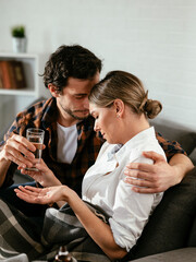 Young woman sick in bed. .Woman drinking medicine, having stomach pain. Husband and wife sitting on sofa.
