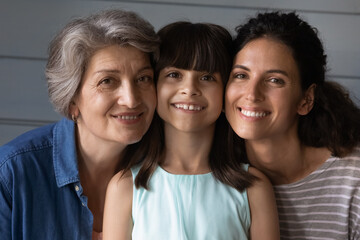 Close up portrait of happy three generations of Hispanic women, child, mom and grandma, pose together. Smiling Latino little girl kid with mother and grandmother show family unity and bonding.